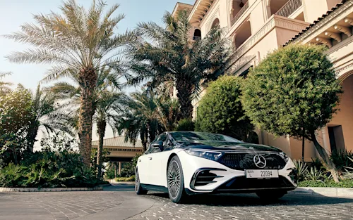 A two-tone Mercedes-Benz EQS parked outside a building with Palm trees out front.