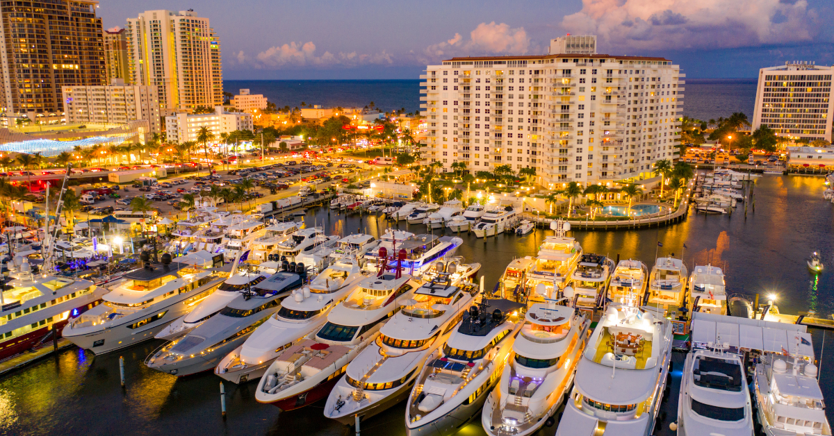 Illuminated yachts at night during the Fort Lauderdale Boat Show with city skyline in the background.