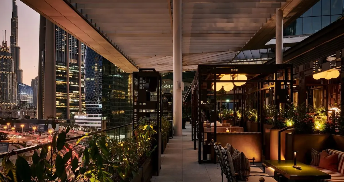 Shot of the rooftop terrace in the Arts Club in Dubai, showing a view of the city at dusk and comfortable seats on the right.