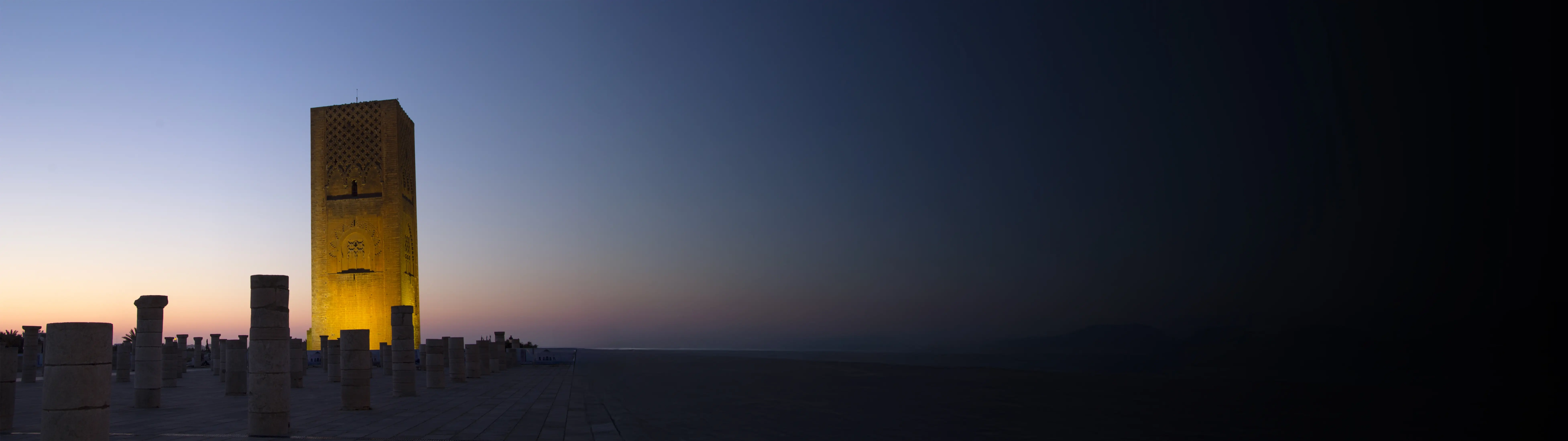 Shot of the Hassan Tower in the Moroccan capital of Rabat, lit up before a dusk sky.