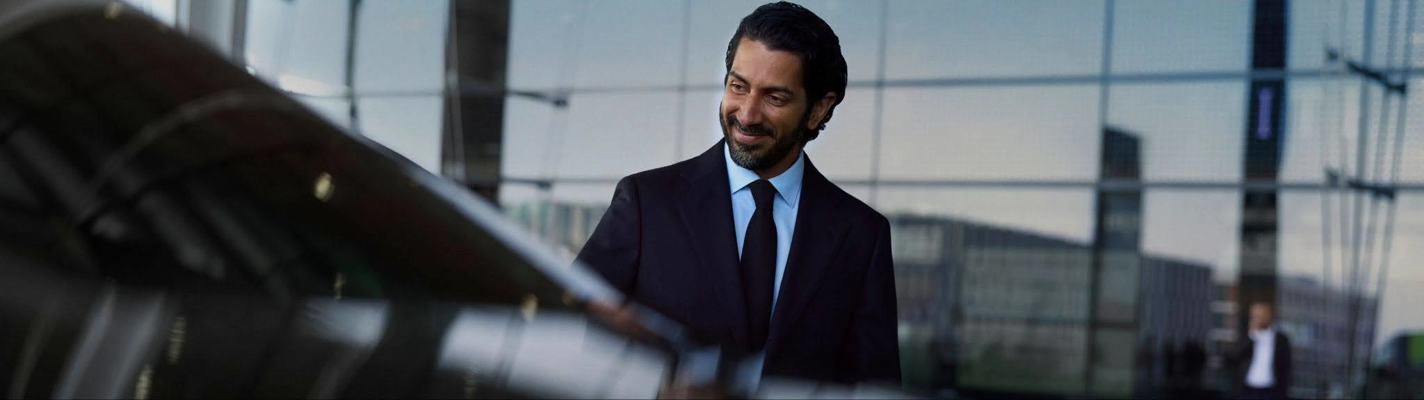 A Blacklane chauffeur smiles while holding a car door open outside an airport.