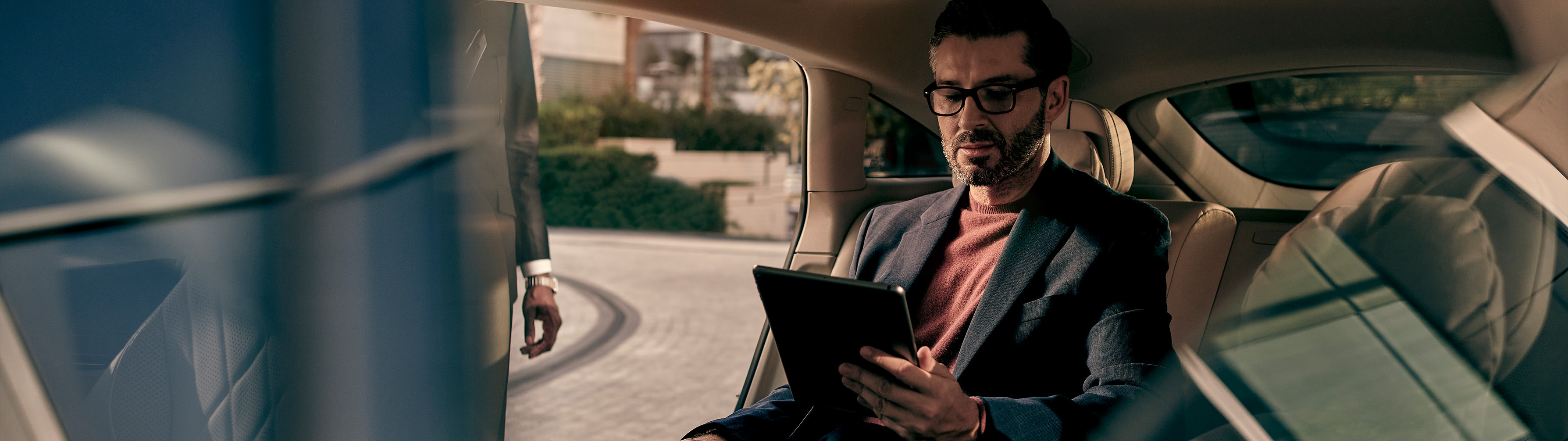 A man using an iPad sits in the back seat of a Mercedes-Benz.