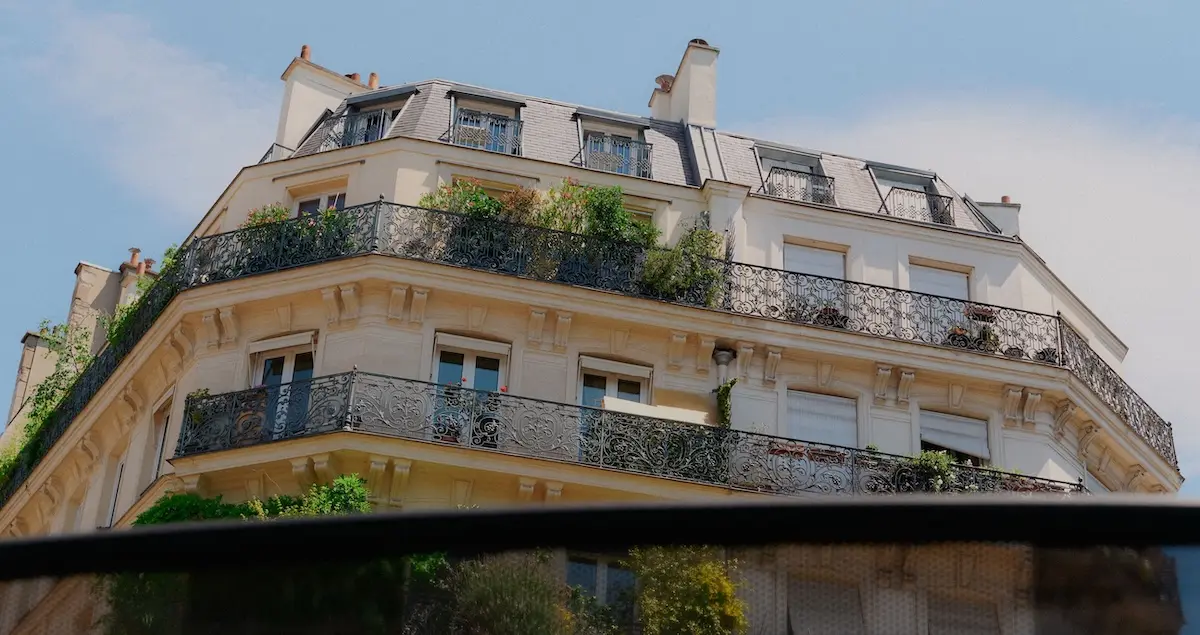 Shot of the upper floor exterior of a Hausmannian building in Paris, taken through the sunroof of a luxury vehicle.