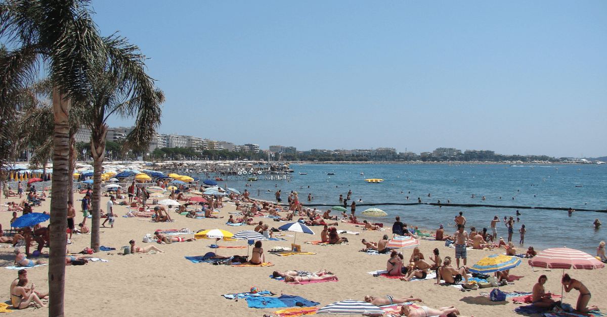 <figcaption class="wp-element-caption">Plage de la Croisette beckons with its golden sands and vibrant beachfront atmosphere in Cannes. <em>Image credit: Wikimedia</em></figcaption>