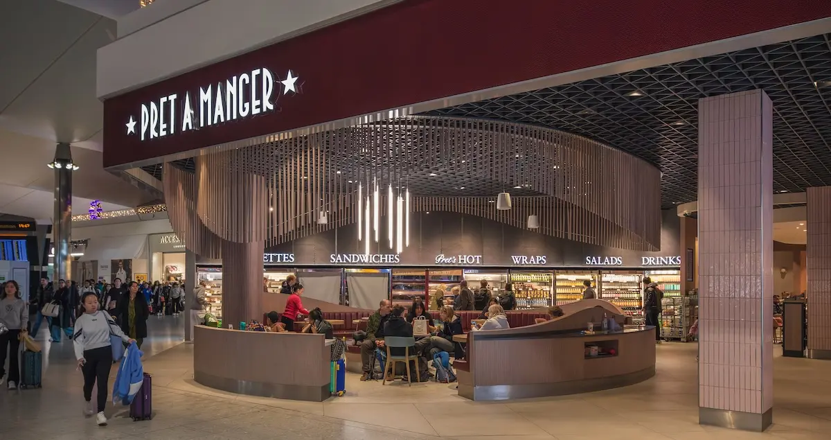 A busy Pret A Manger in a Heathrow airport terminal showing travellers dining and passing.