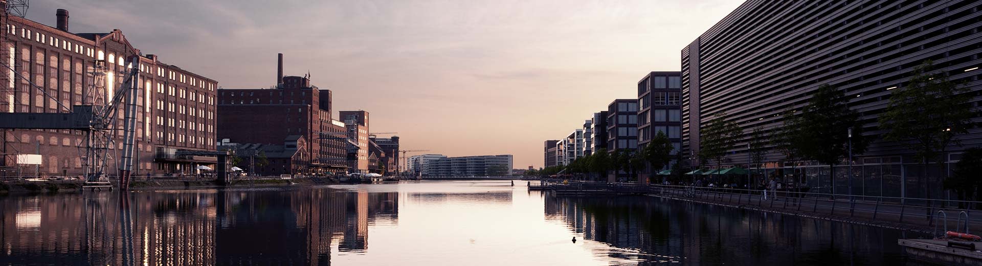 Former industrial buildings of Duisburg set against a dimming sun, with a canal leading to a distant horizon.