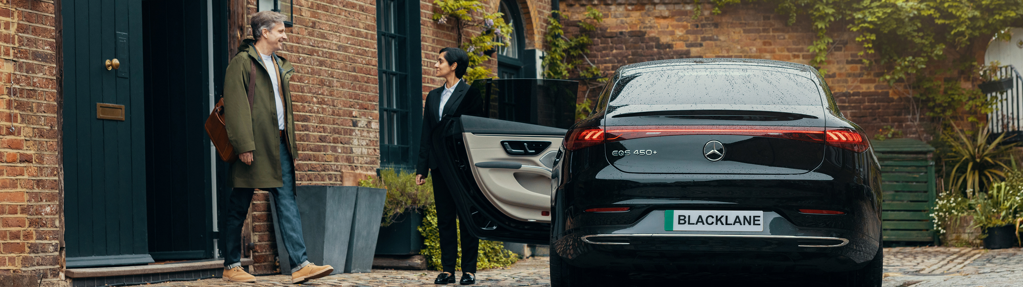 Man steps out the front door of his house to a chauffeur opening the back door to a Blacklane vehicle parked outside.