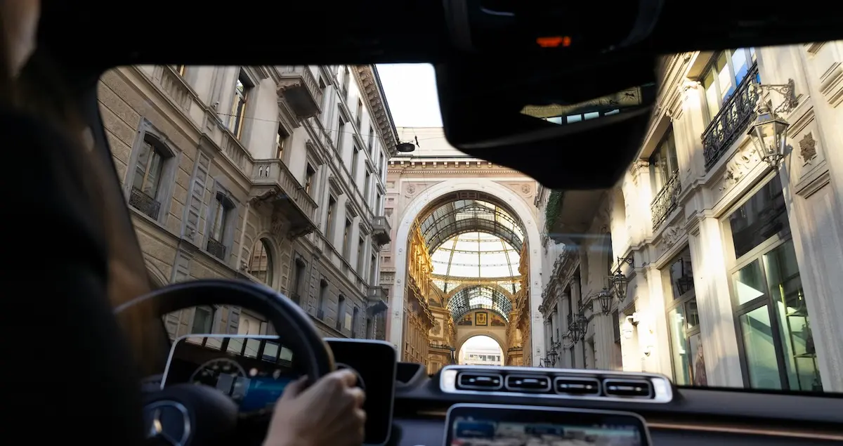 A view of the shopping centre in Milan shot from the backseat of a chauffeured limo, with the dashboard and chauffeur partially in view.