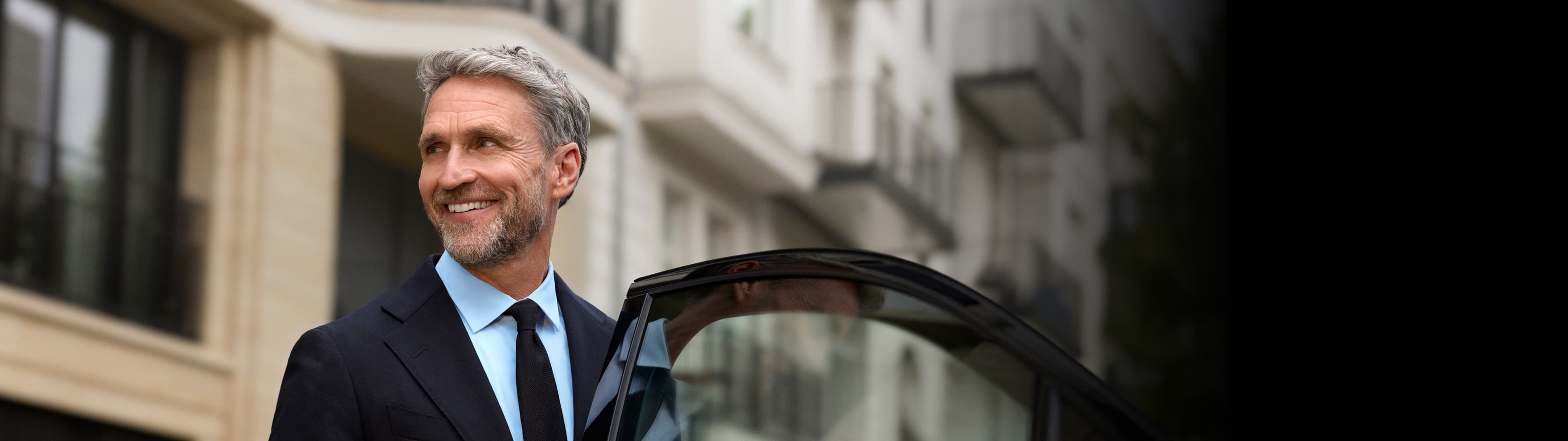 A chauffeur stands smiling beside an open car door.