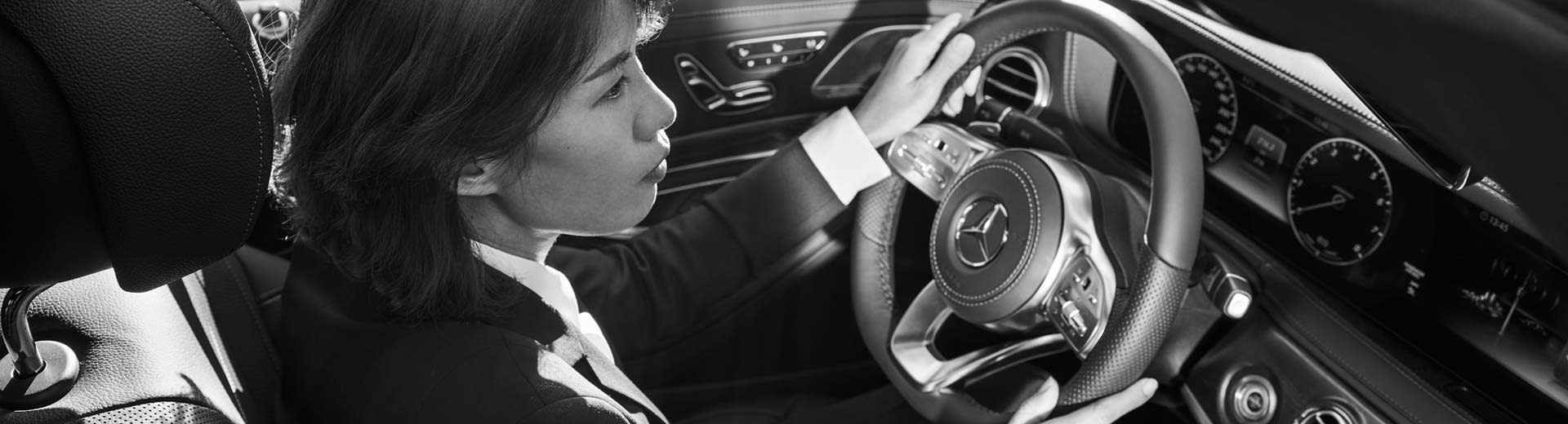Blacklane chauffeur partner Yen sits in the front seat of a Mercedes, both hands on the wheel and focused on the road.