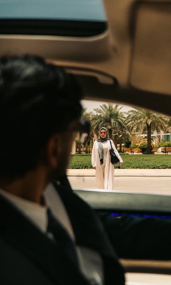 A chauffeur looks out as a woman in a headscarf walks towards the car.