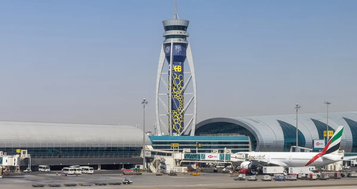 Air traffic control tower at Dubai International Airport, showing terminal buildings on either side.