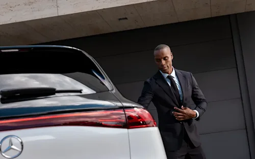 A Blacklane chauffeur about to open the rear door of a two-tone Mercedes SUV.