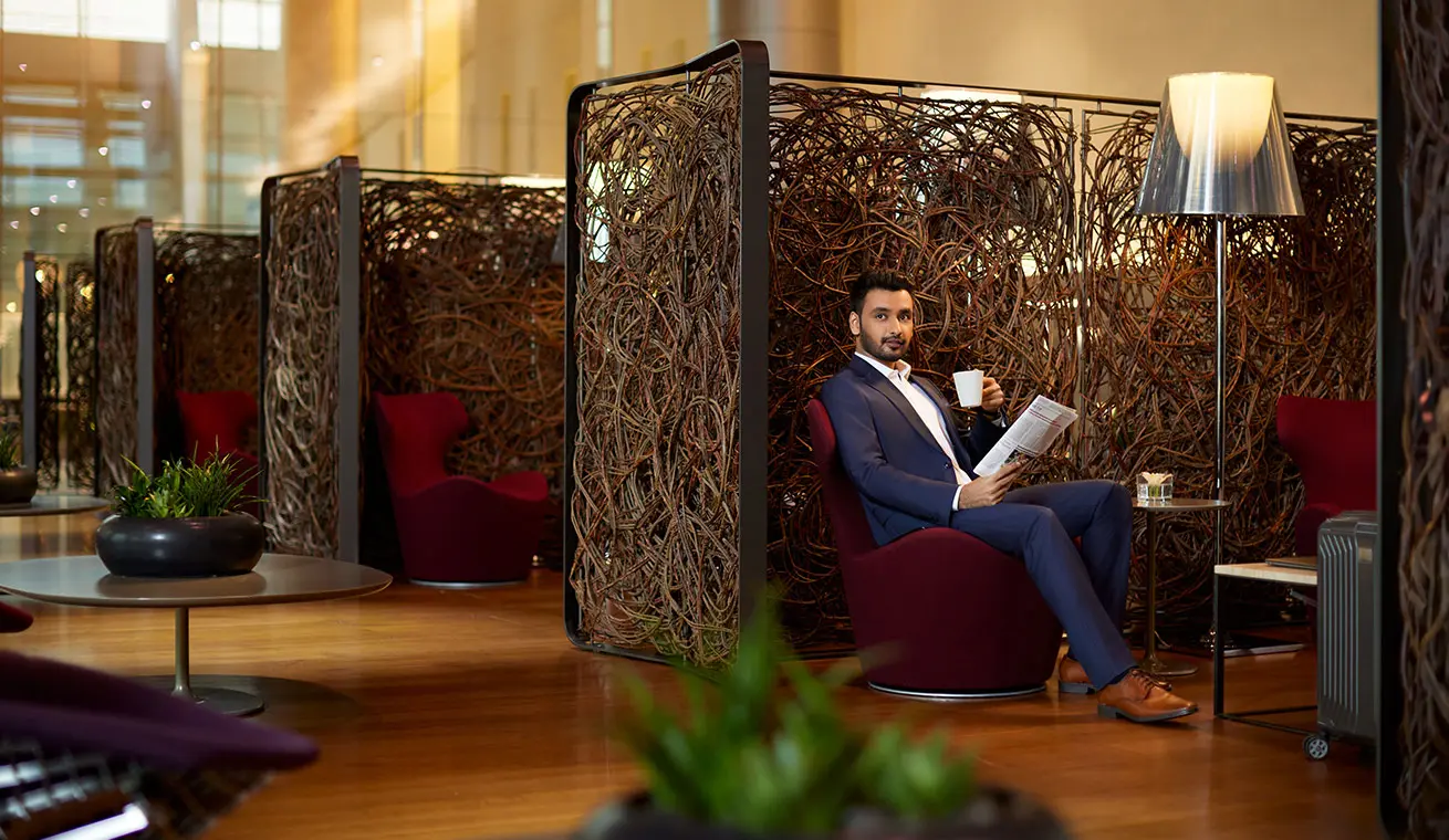 Shot of a businessman reading a newspaper and drinking coffee in the Al Mourjan Business Lounge - South at Doha Airport.