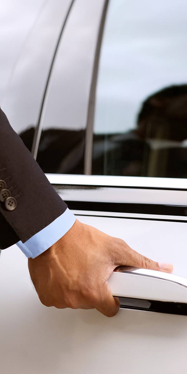 A chauffeur's suited hand pulling the handle of a two-tone Blacklane limousine.