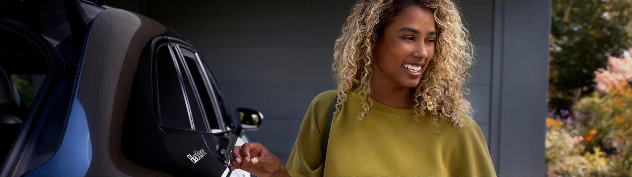 A stylish woman stands about to get into a two-tone Blacklane Mercedes car.