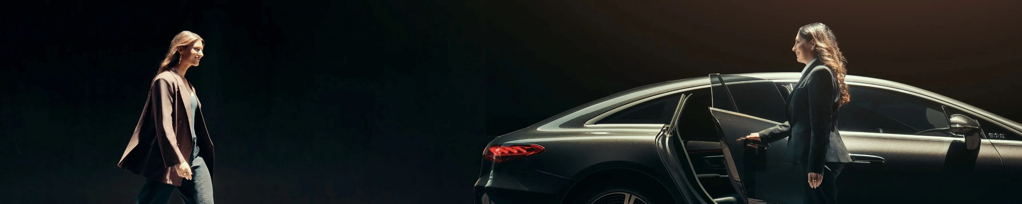 A stylish woman walks towards a sleek Blacklane Mercedes limo, with her chauffeur holding the door open.