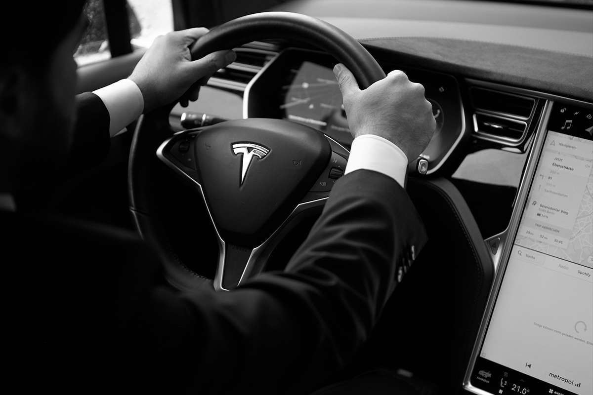 A Blacklane chauffeur with his hands on the wheel, with the Tesla logo and high-tech dashboard visible.
