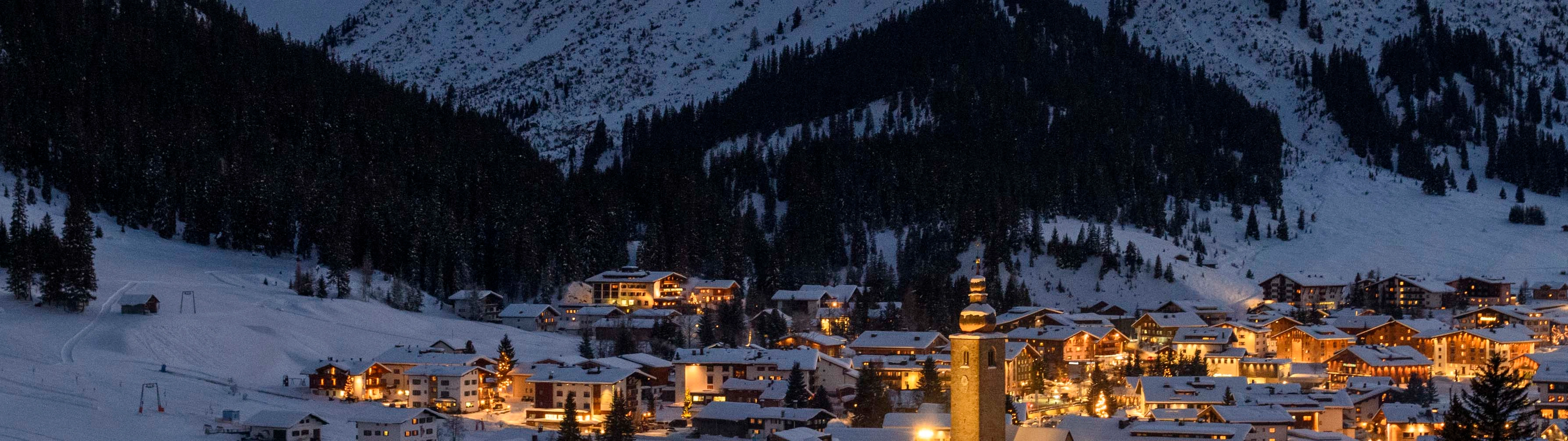The beautiful village of Lech am Arlberg lights up the cold night sky, surrounded by snow-packed slopes.