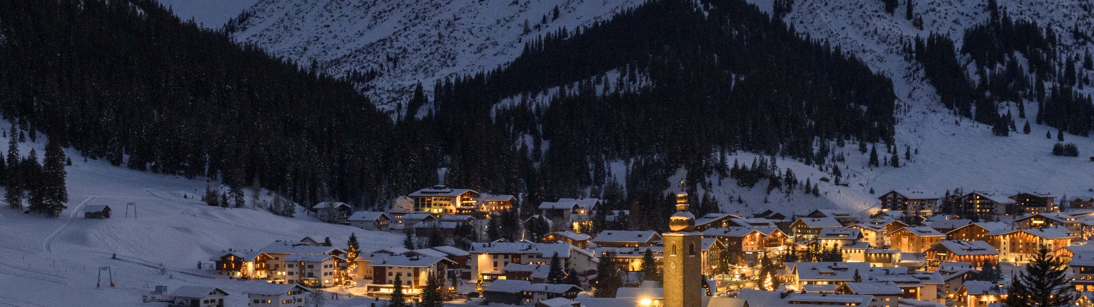 The beautiful village of Lech am Arlberg lights up the cold night sky, surrounded by snow-packed slopes.