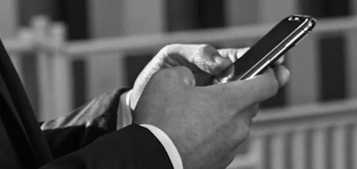 Un hombre con un buen traje sujeta un móvil con ambas manos, mientras usa la app para reservar un traslado.