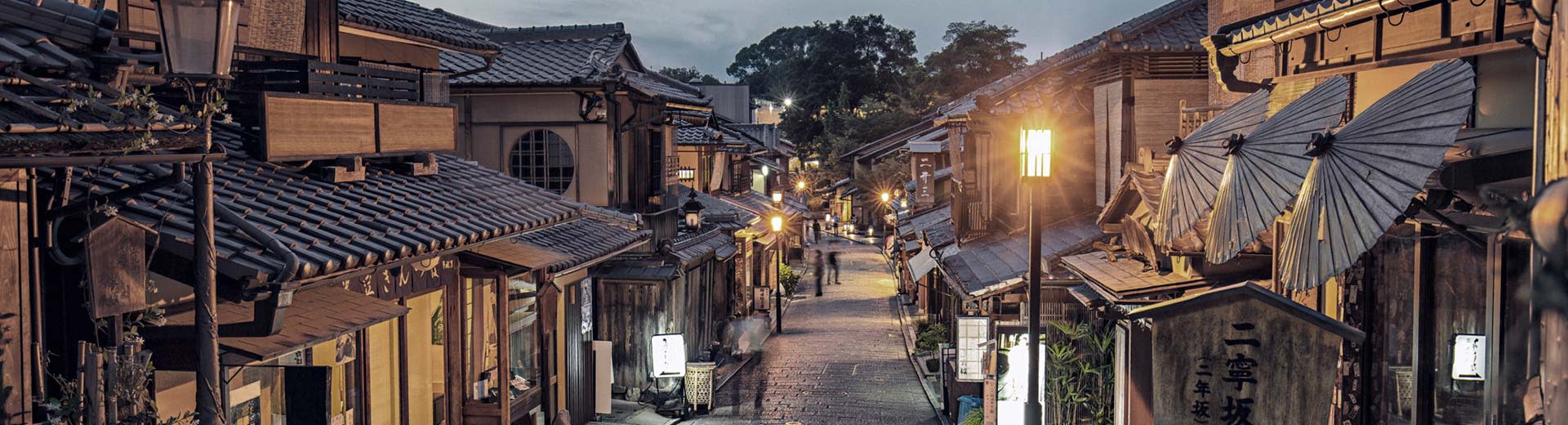 In evening light a narrow street lined with old buildings with wooden facades in Kyoto.