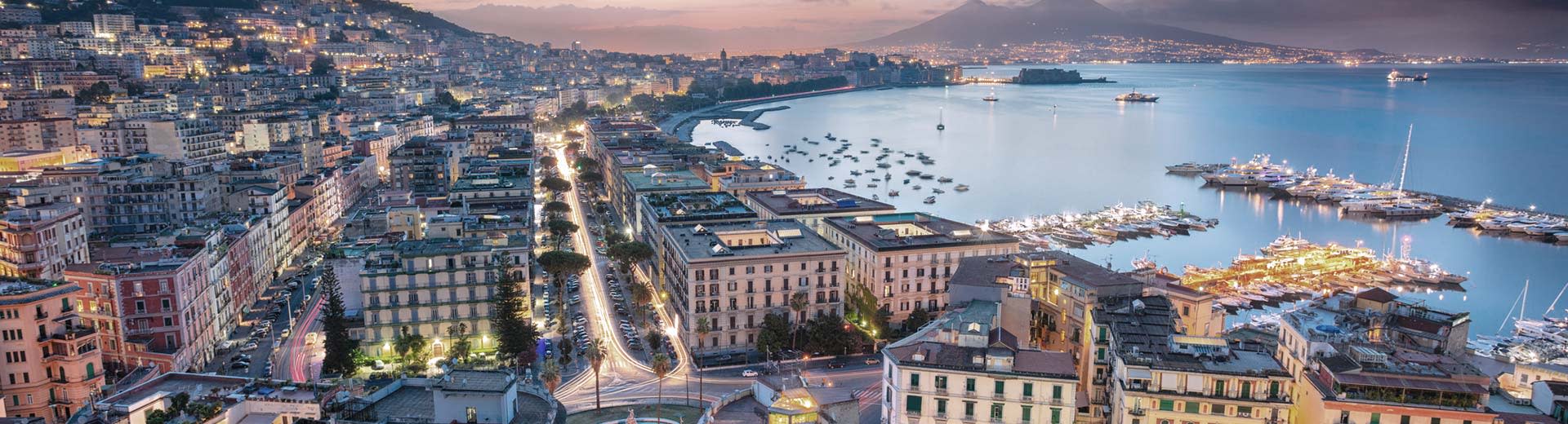 Die schöne Stadt Neapel erstreckt sich in der Abenddämmerung über die Küste, wobei der Ozean im Hintergrund liegt.