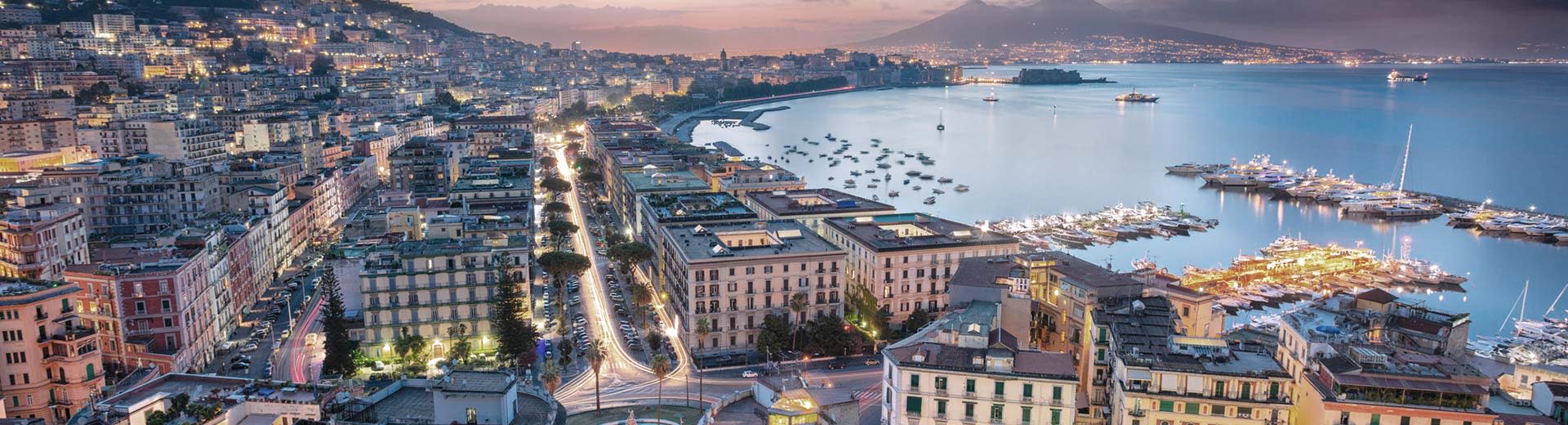 La belle ville de Naples s'étend à travers la côte au crépuscule, avec l'océan gisant en arrière-plan.