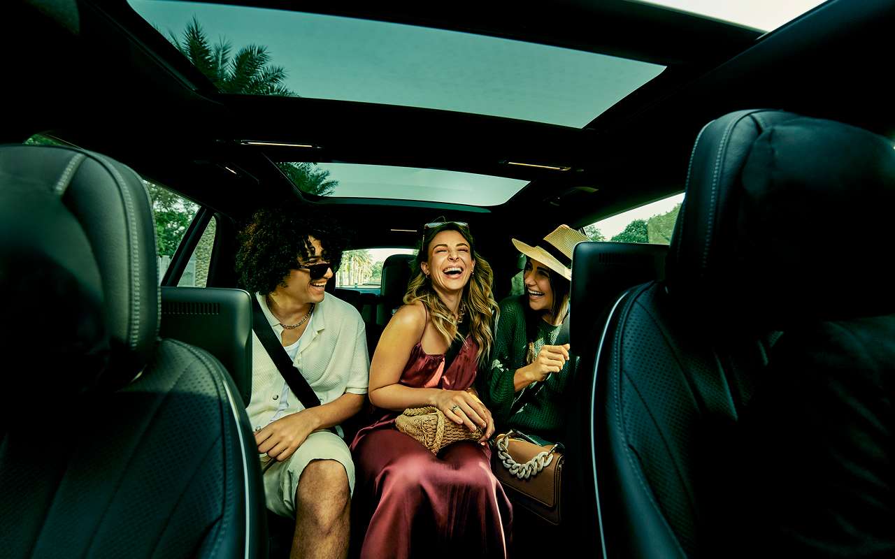 Shot of three young people sitting in the back seat of a Blacklane limo going to a concert.