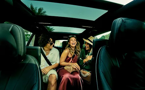 Shot of three young people sitting in the back seat of a Blacklane limo going to a concert.