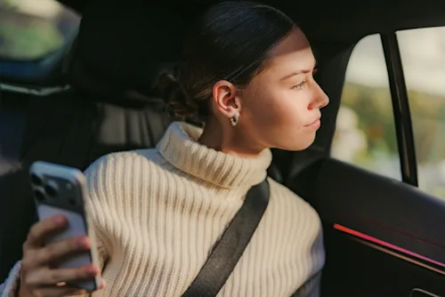 A woman looks out of a Blacklane car while holding her phone.