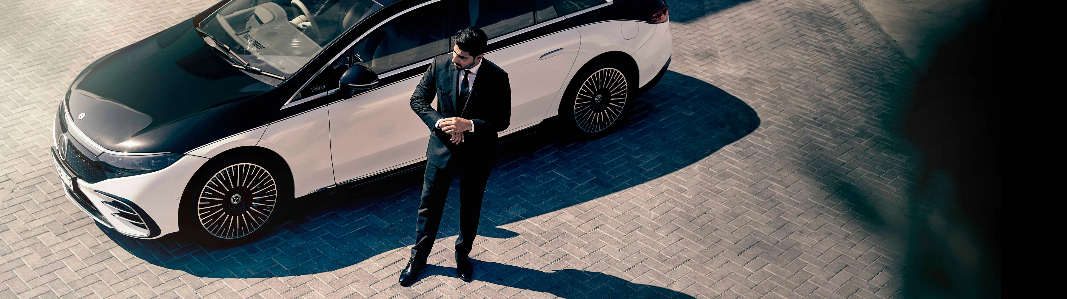 Chauffeur checks watch in front of black and white Mercedes EQS.