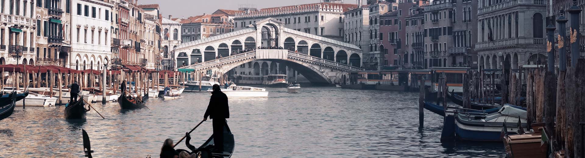 Las vías fluviales de Venecia están llenas de góndolas y sus pasajeros, mientras que en el fondo se encuentran una hermosa arquitectura.