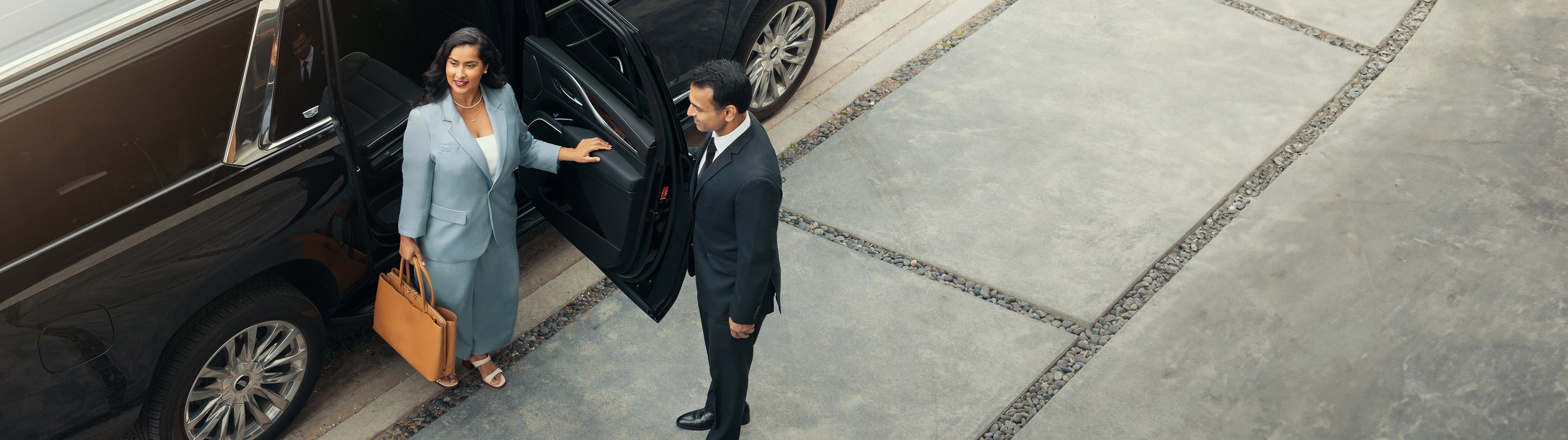 A woman looks around as she emerges from her vehicle, with a chauffeur opening the door.