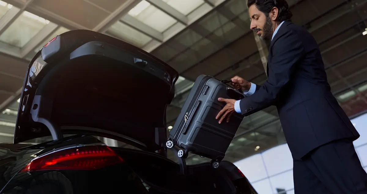A suited Blacklane chauffeur places a travel case into the boot of a Blacklane car service outside an airport.