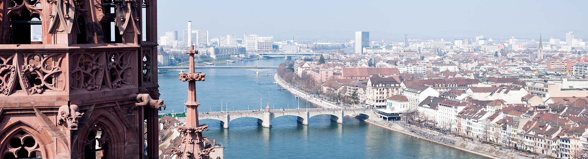 Birds View de la rivière Rheine à Bâle par une journée ensoleillée, avec une tour partiellement en vue sur la gauche et trois ponts qui traversent la rivière.