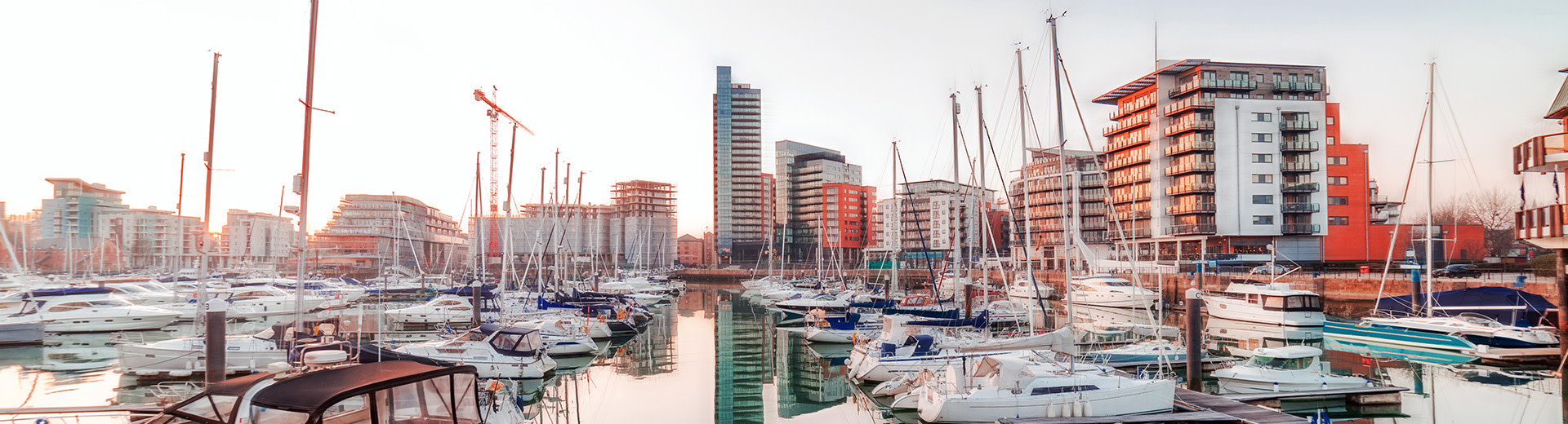 A twilight picture of a marina in Southampton, with several moored yachts. The image of residential buildings in the background is reflected on the water.