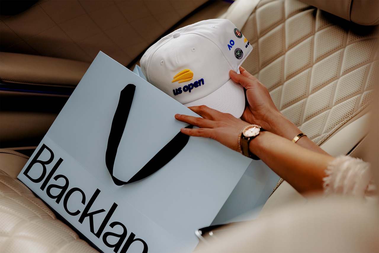 A hand holds a US Open hat with a Blacklane gift bag in the back seat of a Blacklane limo.