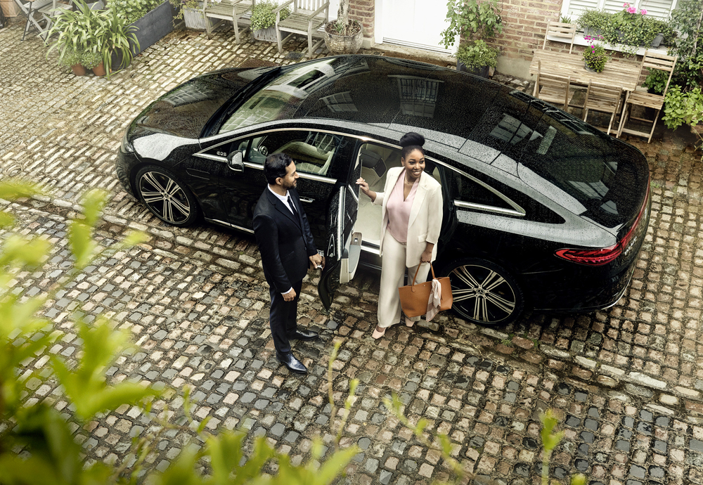 A Blacklane chauffeur opens the door for his guest who steps out in a white suit.