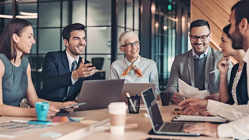 A group of professionals with laptops speaking at a table.