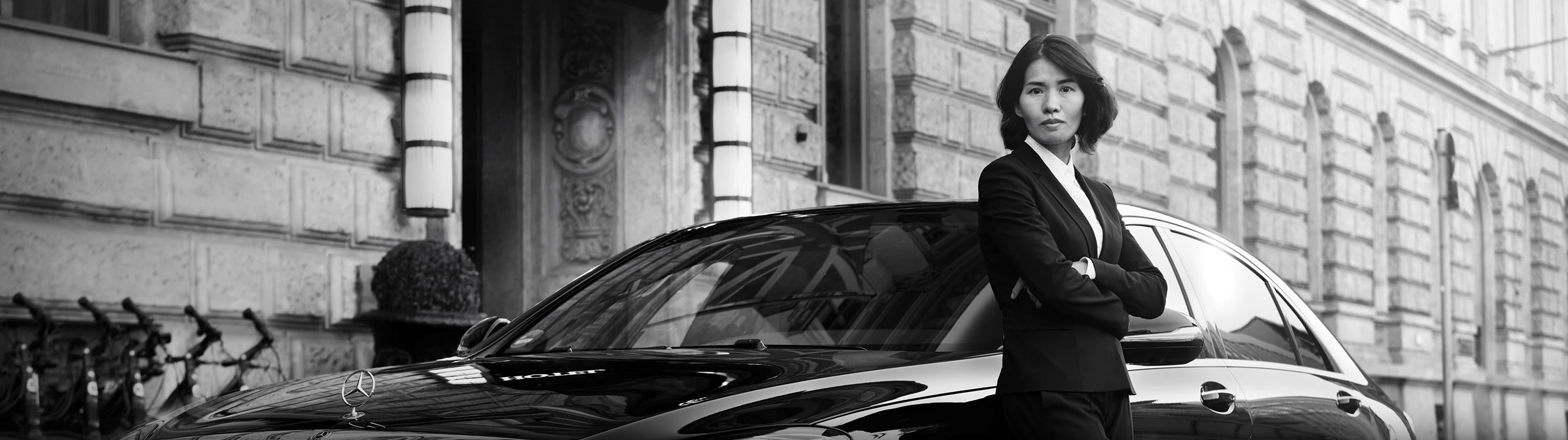 Real Blacklane chauffeur Yen stands in front of her vehicle wearing a suit.