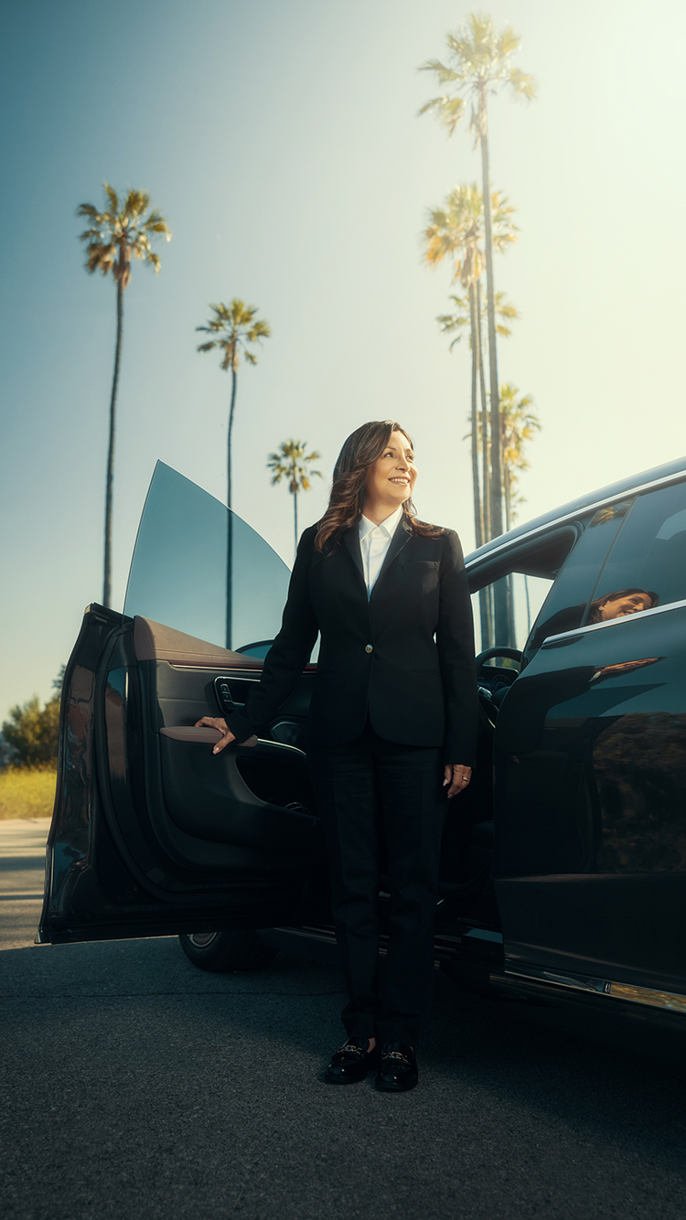 A chauffeur smiles as she gets out of her vehicle with palm trees in the background.