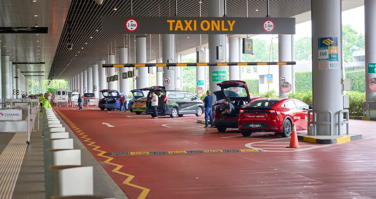 Taxi drivers loading luggage into cars at Singapore Changi airport pickup area.