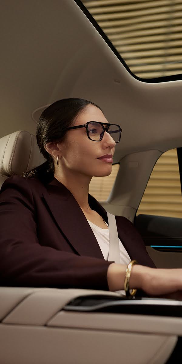 A smartly dressed woman with designer glasses sits in the backseat of a Blacklane limousine.