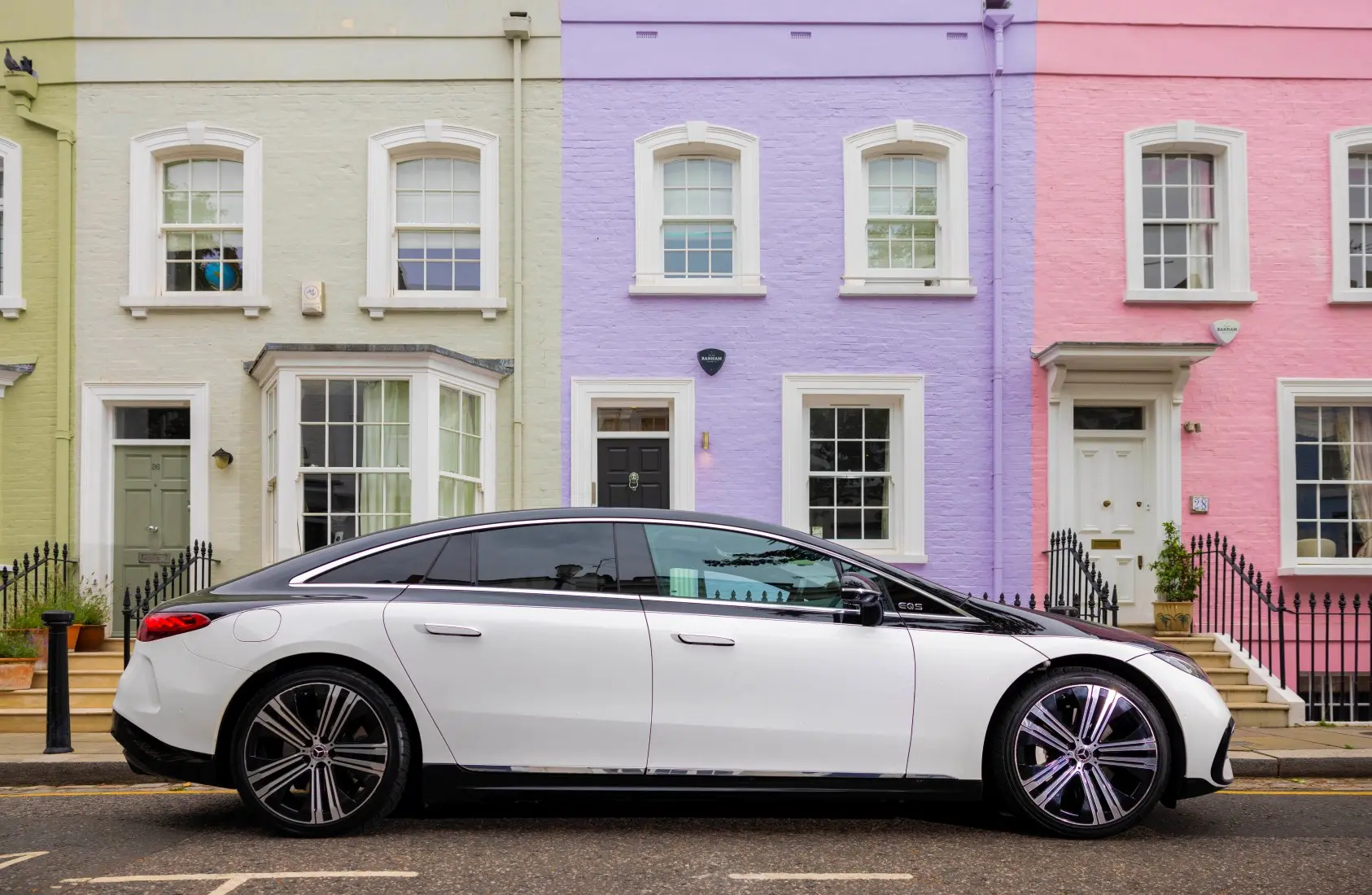 A sleek two-tone Blacklane Mercedes EQE parked on a colourful London street.