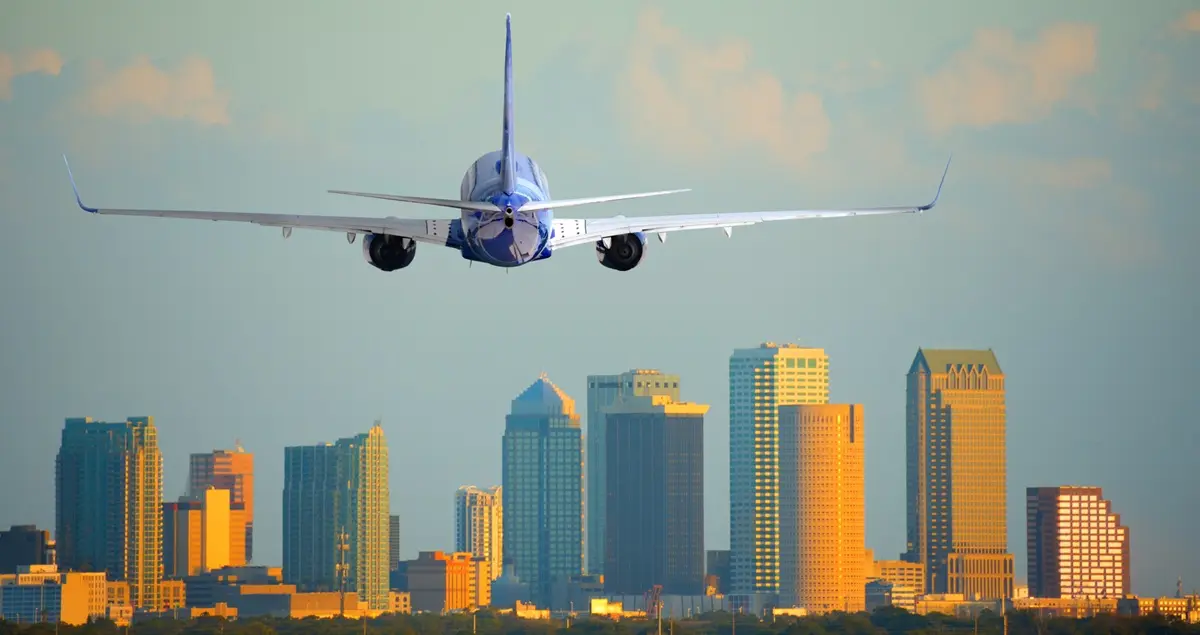 Passenger jet plane departing Tampa International Airport in Florida at sunset or sunrise with the downtown skyscrapers in the background.