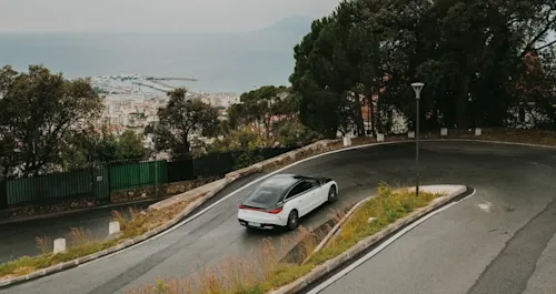 A Blacklane two-tone Mercedes limo travels up a hairpin bend on the Cote d'Azur with a city and harbour in the background.