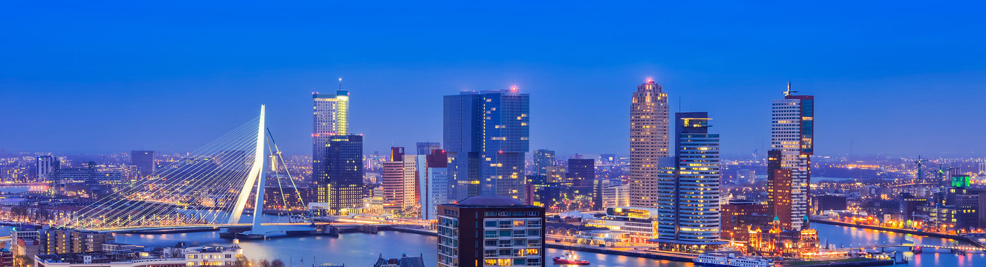 藍色の空を背景に、夕暮れの光に照らされたロッテルダムのスカイライン。