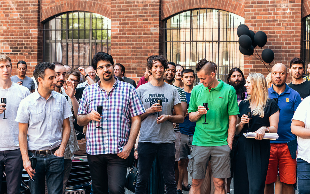 A big crowd of employees gathered in the courtyard and holding black champagne flutes at a company event.