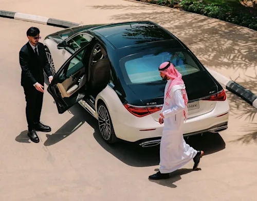 A man in traditional Saudi dress entering a Mercedes EQS limo while the chauffeur holds the door open for him.